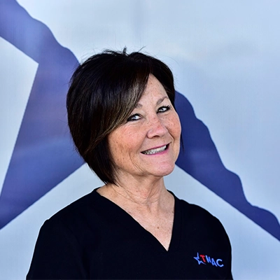 Patient Financial-Insurance Specialist Keri Morton Smiling In Front Of Logo Backdrop