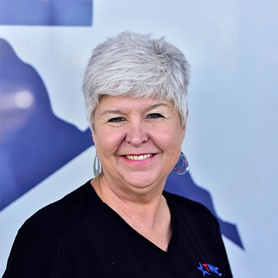 Front Desk Associate Sherry Thomas Smiling In Front Of Logo Backdrop