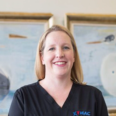 Chiropractor Cari Guidry Smiling In Front Of Office Artwork